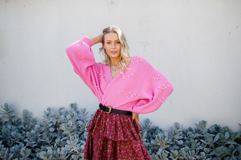 Rhiannon wears the Bowie Bobble knit cardigan in cosmic pink, she is wearing it as a wrap with a floral skirt and belt.